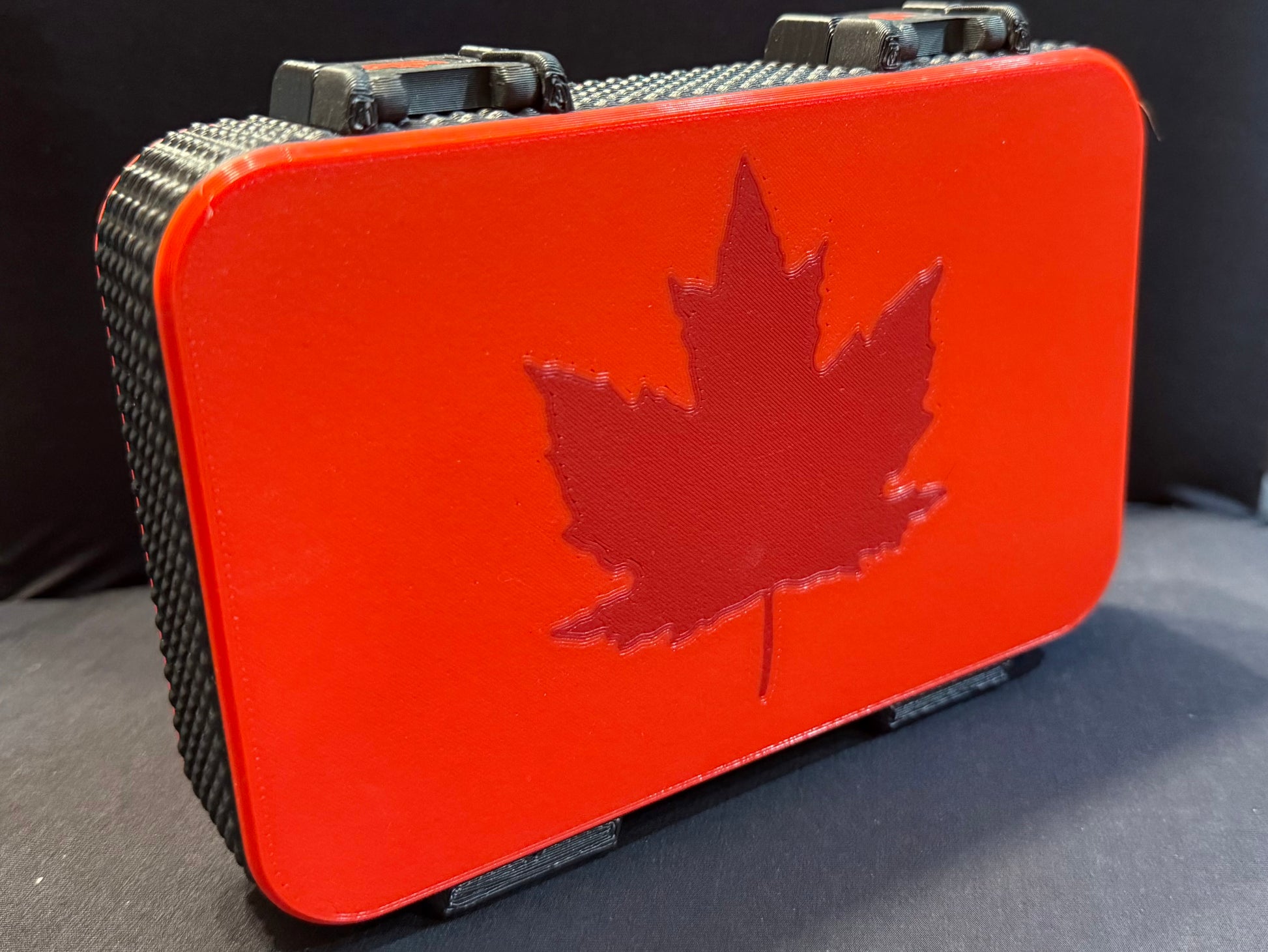 Front view of Canadian-made harmonica case in light-red, black, with a dark-red embossed maple leaf design.